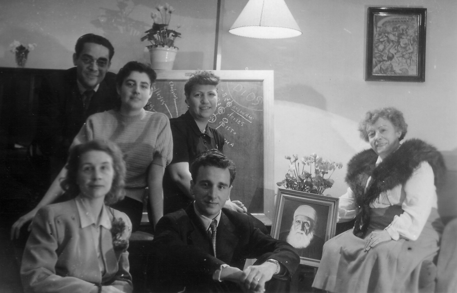 Fotografía en blanco y negro de creyentes bahá’ís en los primeros años de la Fe Bahá’í en España, reunidos junto a un retrato de ‘Abdu’l-Bahá.